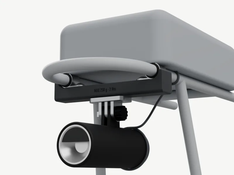 Render from front-left, just below the rails: a grey box bag on the platform and, under the two top rails, a charcoal beam, MAX 250 g · 2 Nm on its side, held by two rubber-lined stainless P-clamps. An aluminium GoPro 3-prong under the beam carries a black round lamp ahead of the bag, reflector forward, with a cord from the lamp to the left rail.